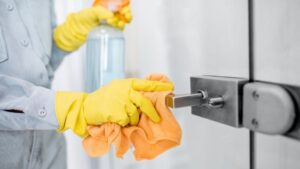 Person cleaning a door handle with a spray bottle and cloth, emphasizing hygiene and maintenance of door hardware.