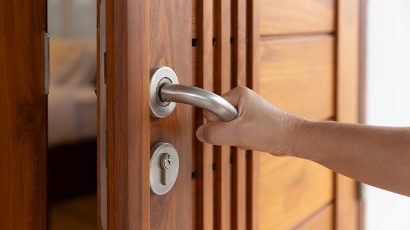 A person opening a wooden door with a modern silver door handle in a cozy, natural interior setting. Sustainable, stylish, and eco-friendly home design emphasizing quality craftsmanship.